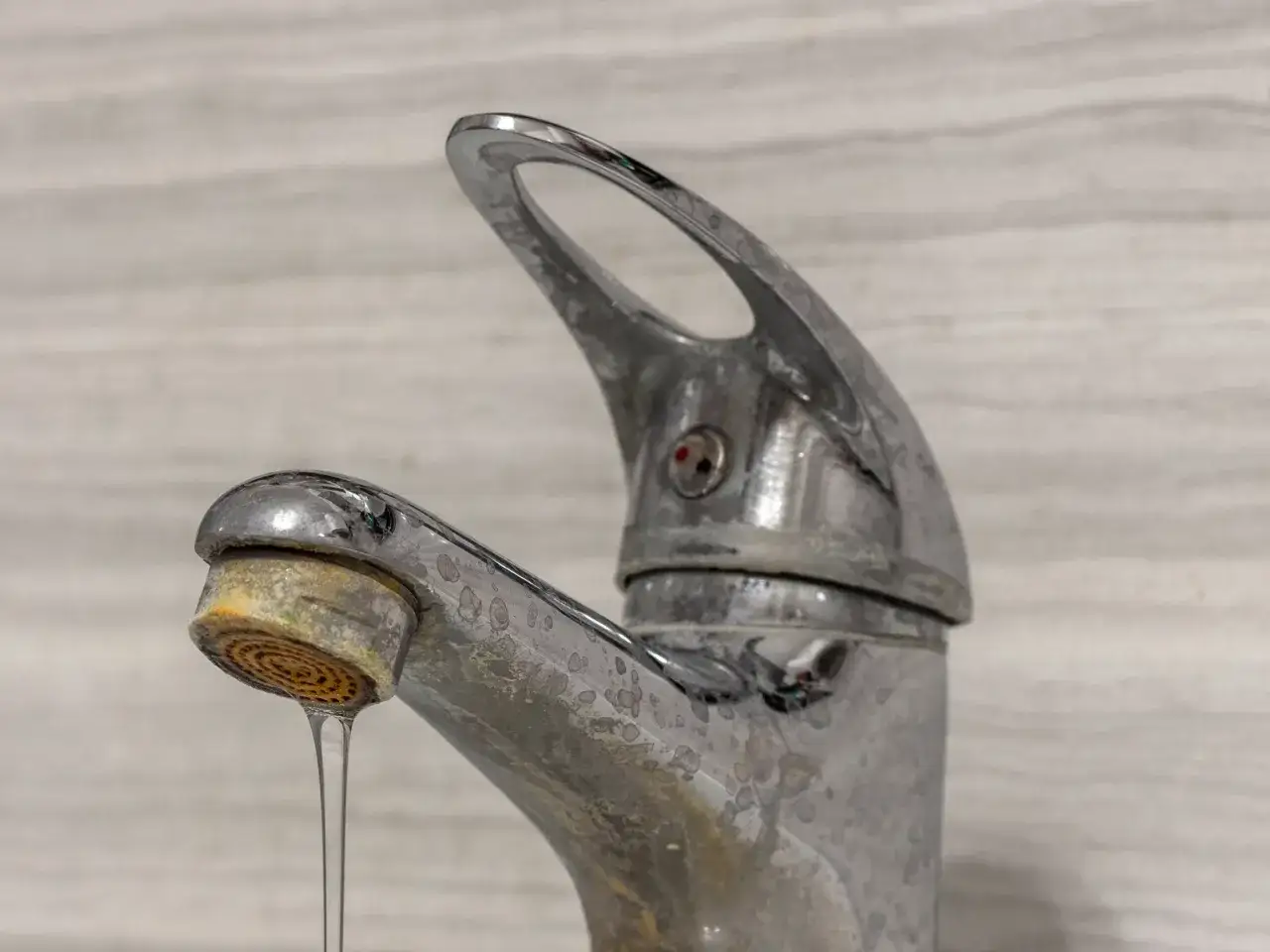 Zabrudzony kamieniem kran z kapiącą wodą.