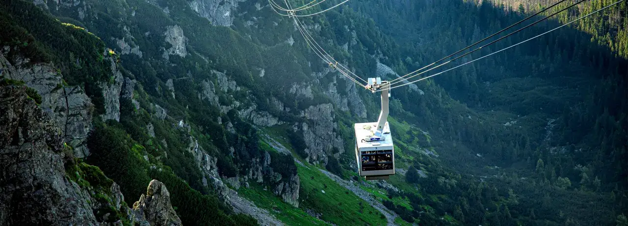 Kolejka linowa w Tatrach na tle skalistych zboczy i lasu.