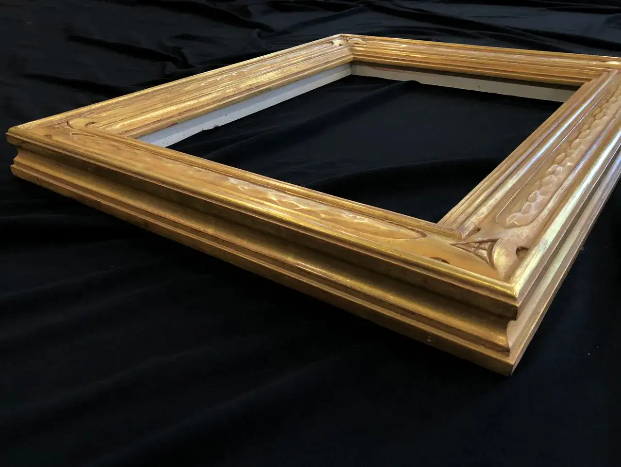 Złota, ozdobna rama obrazu czeka na renowację. Jej bogate zdobienia i wyrazisty kształt sugerują, że jest gotowa na nowe życie.