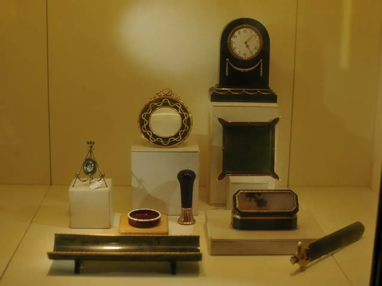 Eksponaty muzealne: zegar, ramka, szkatułka, ozdobny stojak i inne przedmioty, przypominające dzieła sztuki Fabergé.