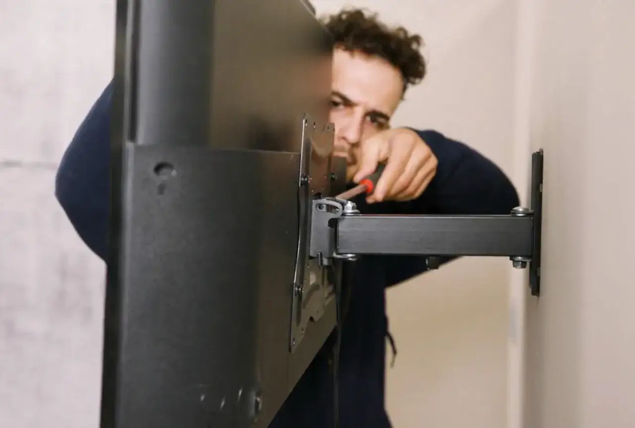 Mężczyzna dokręca śruby podczas montażu TV na ścianie. Widać uchwyt i fragment telewizora.