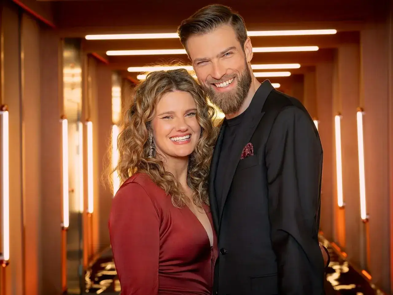 Uśmiechnięta para w eleganckich strojach, ona w czerwonej sukni, on w czarnym garniturze. Ich spojrzenia mówią wszystko – miłość jest ślepa, ale szczęśliwa.