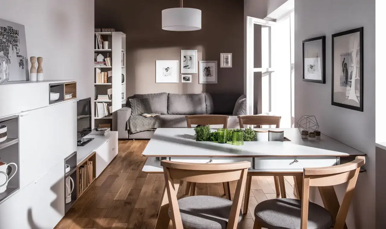 Mała jadalnia inspiracje: nowoczesny salon z szarą kanapą, białymi meblami i drewnianym stołem.