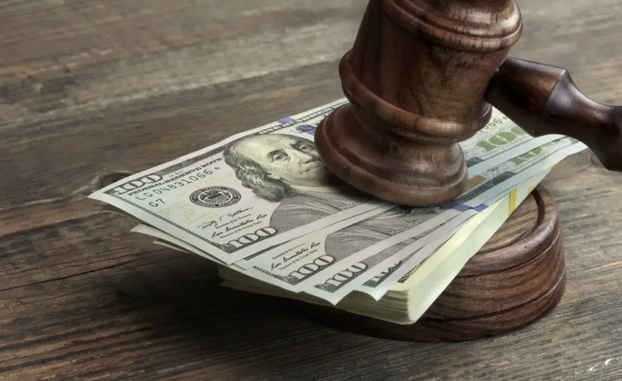 Młotek sędziowski na stosie banknotów 100-dolarowych. Pytanie: ile procent bierze prawnik od wygranej sprawy?