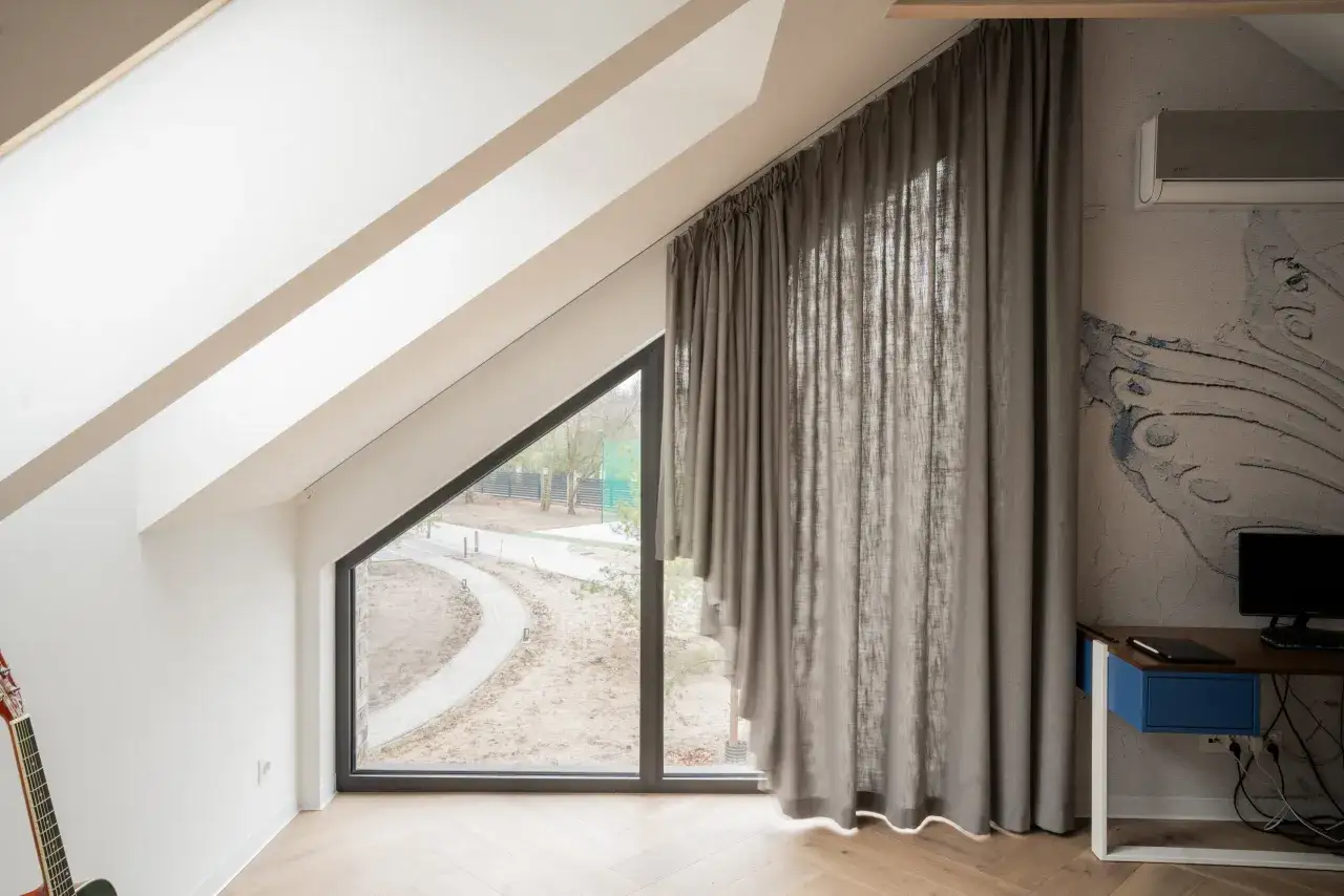 Eleganckie karnisze na skośne okna idealnie komponują się z szarymi zasłonami, tworząc przytulną atmosferę w pokoju na poddaszu.