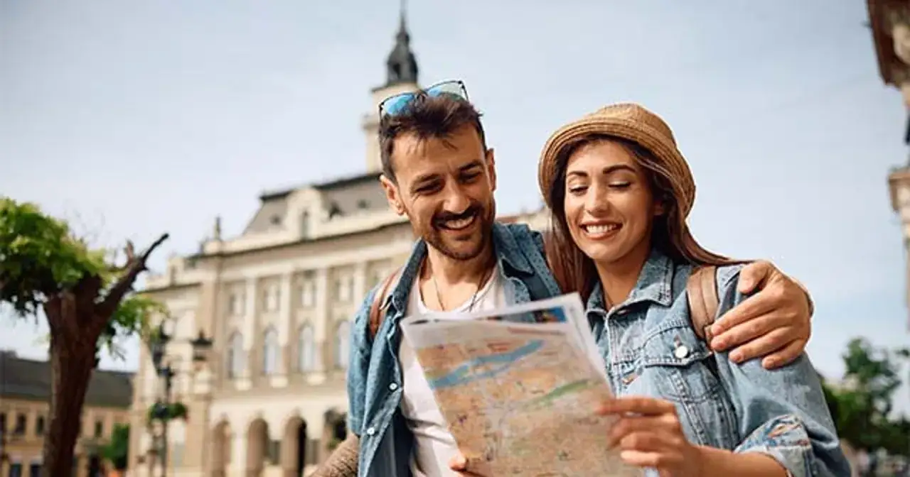 Uśmiechnięta para planuje wyjazd na weekend, studiując mapę na tle zabytkowej architektury.