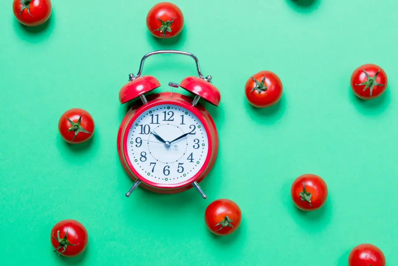Czerwony budzik i pomidorki na zielonym tle. Czy to symbol techniki "pomodoro" do efektywnej pracy?