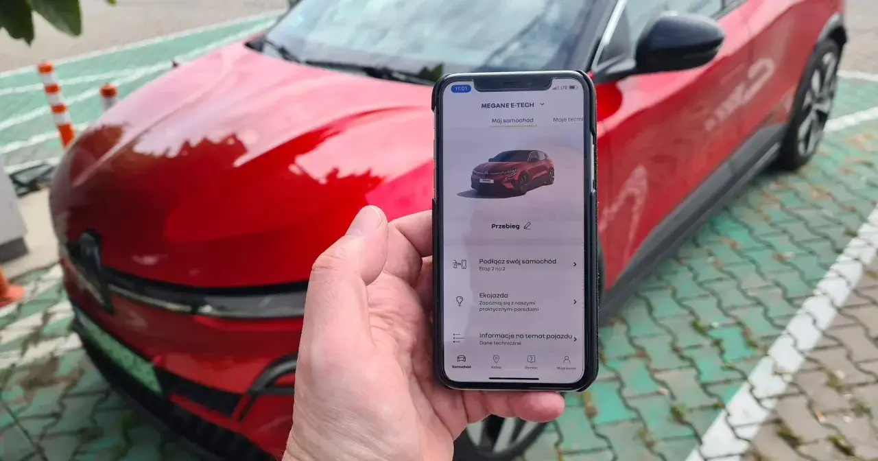 Aplikacja na telefonie pokazuje, jak przerobić auto na elektryczne, obok czerwonego samochodu.