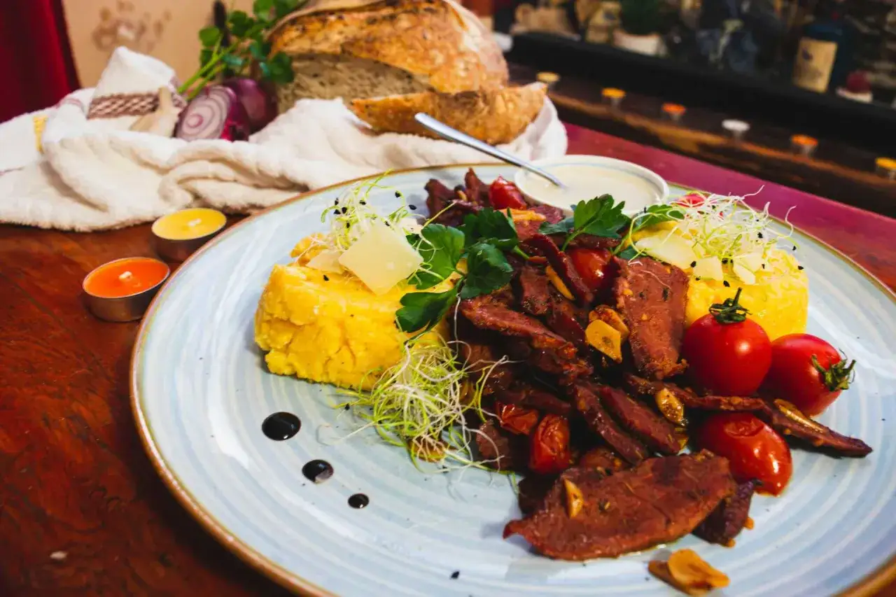 Pyszne jedzenie w Rumunii: polenta z wołowiną, pomidorkami i serem. Obok świeży chleb i świece tworzą przytulną atmosferę.