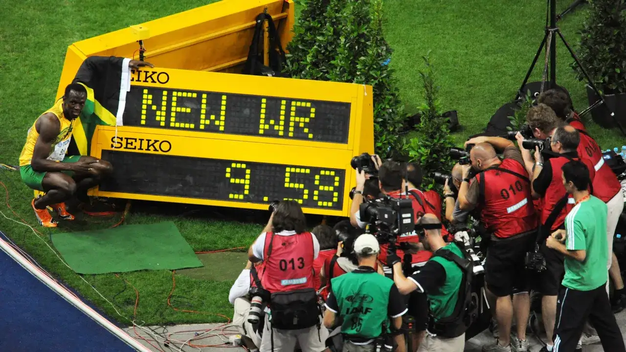 Usain Bolt, najszybszy człowiek świata, świętuje nowy rekord świata 9.58s. Otoczony przez fotoreporterów, z flagą Jamajki.