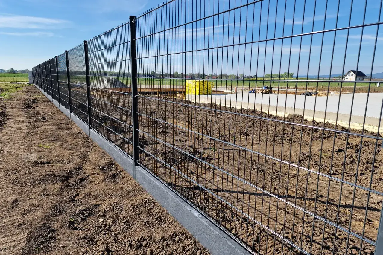 Nowy, metalowy płot panelowy z betonowym podmurówką na budowie.