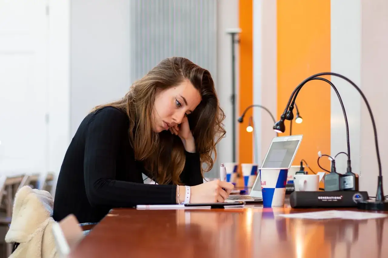 Młoda kobieta pochylona nad notatkami, szukająca sposobów, jak się lepiej uczyć. Obok laptop i kubek z logo Red Bull.