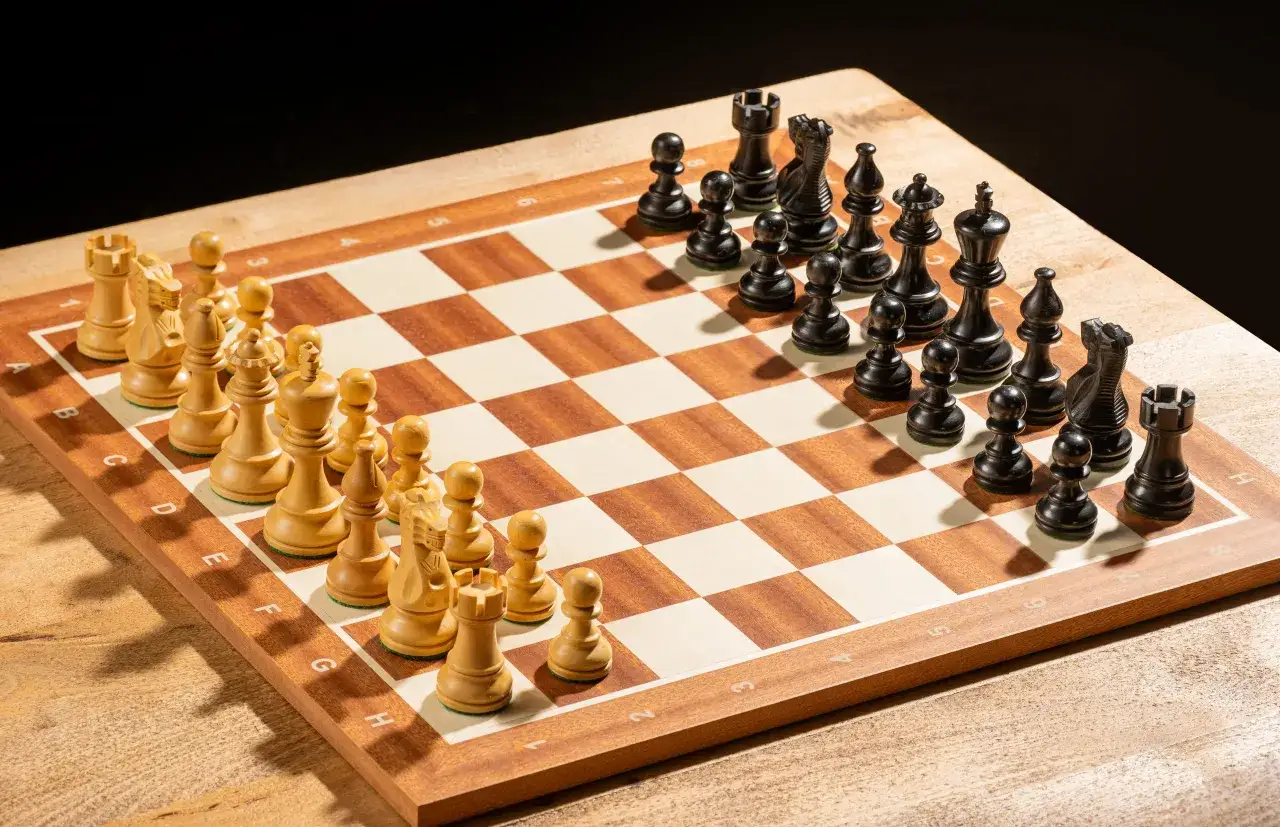 Drewniana szachownica z ustawionymi białymi i czarnymi figurami szachowymi.