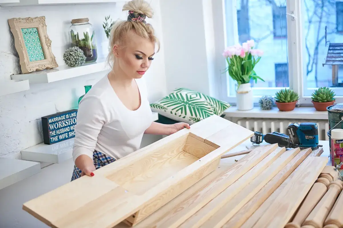 Kobieta składa drewniany stół, obok narzędzia i deski.