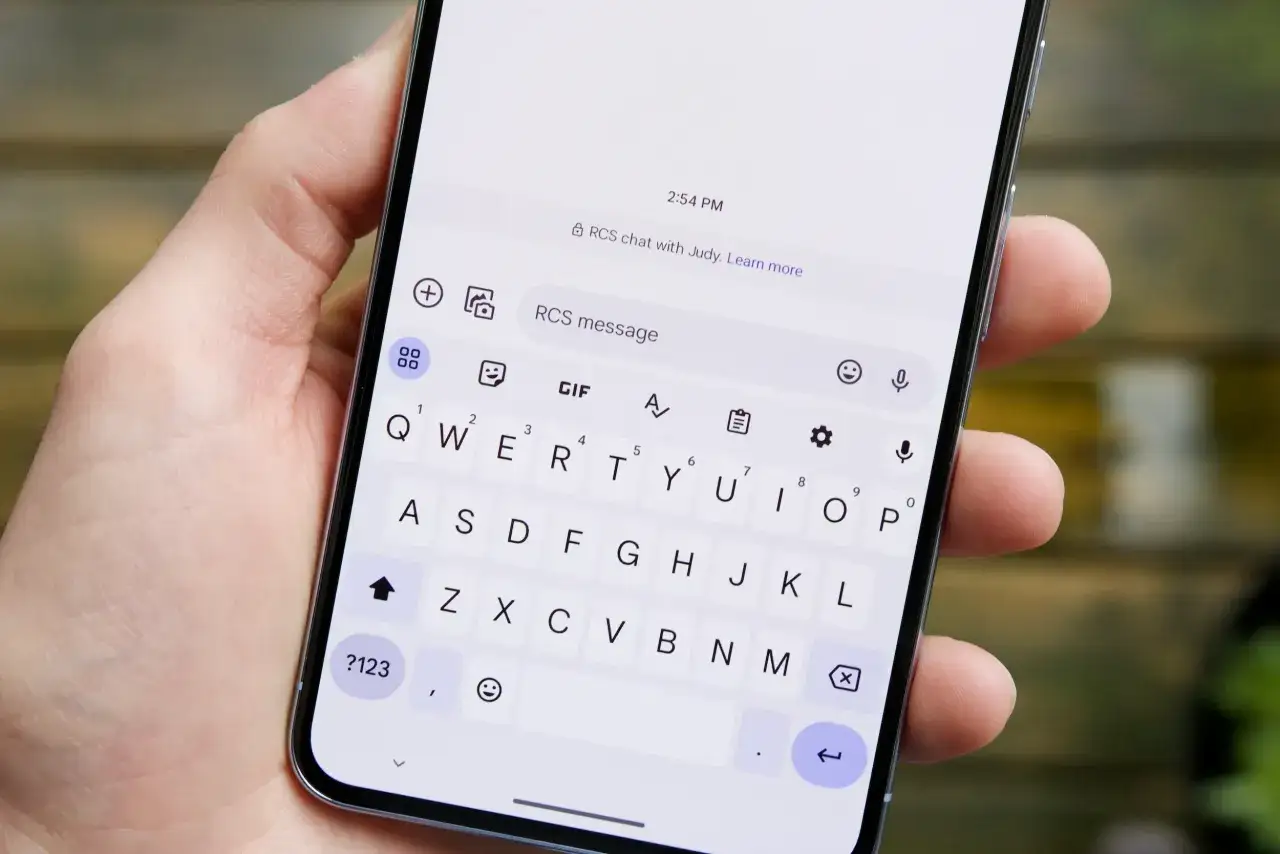 Dłoń trzyma smartfon z otwartą klawiaturą. Na ekranie widać informację "RCS chat with Judy", co wyjaśnia, rcs co to jest.