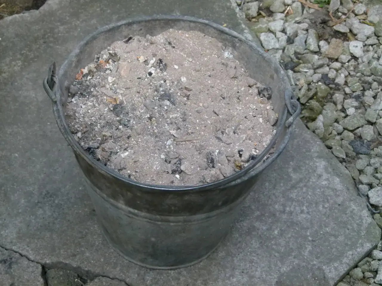 Metalowy kubeł wypełniony popiołem z węgla, który może posłużyć jako cenny nawóz do ogrodu.