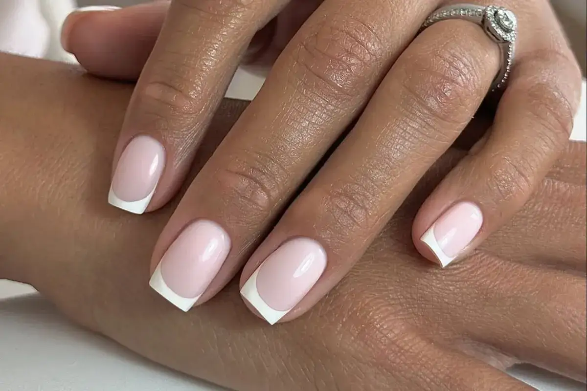 Delikatny french manicure z różowymi paznokciami, jak płatki kwiatów. Na serdecznym palcu błyszczący pierścionek.