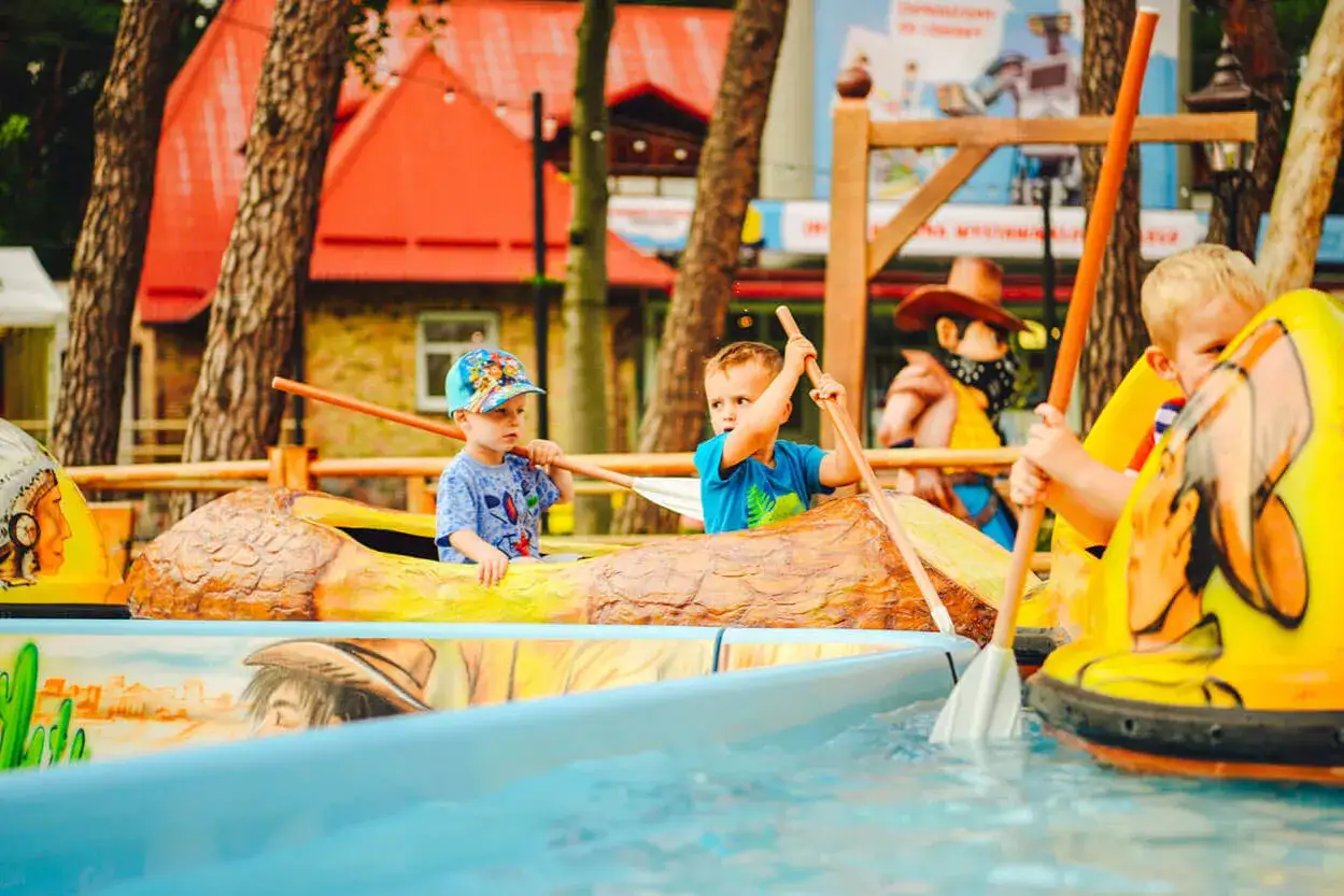 Dzieci wiosłują w łódkach w kształcie kłód i żółtych łodzi na wodzie w Discovery Park Łeba.