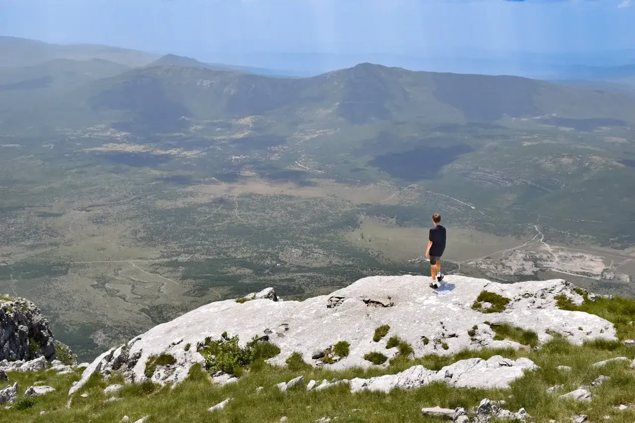 Chłopiec stoi na skalistym szczycie, podziwiając rozległy krajobraz gór Dynarskich.