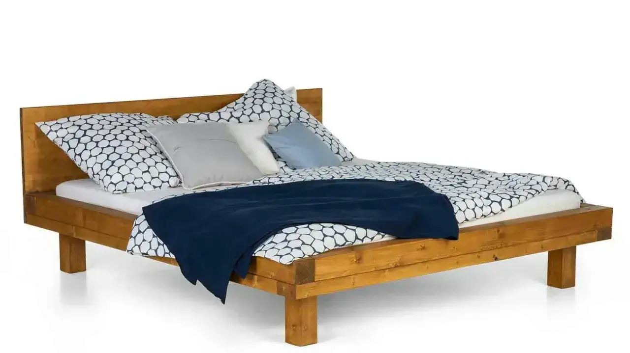 Drewniane łóżko z pościelą w geometryczny wzór i granatowym kocem. Inspiracja, jak obić łóżko materiałem, by nadać mu nowy wygląd.