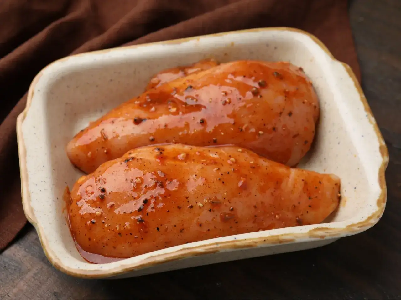 Dwa surowe filety z kurczaka w marynacie w naczyniu żaroodpornym.