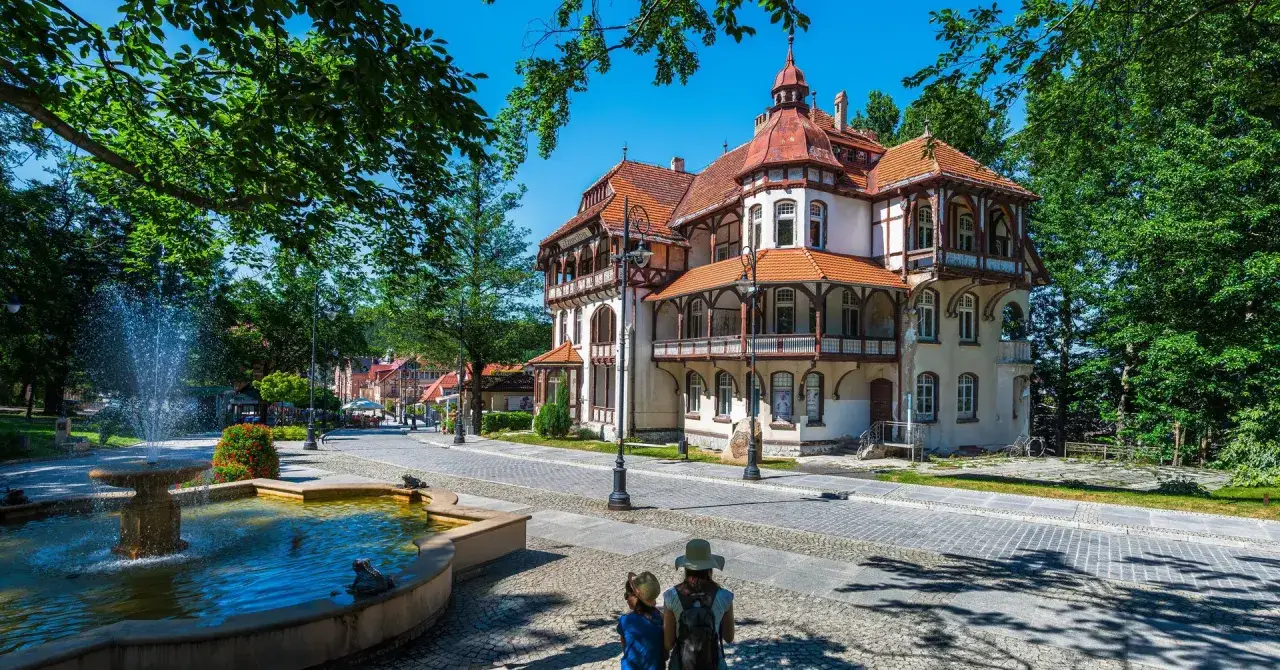 Architektura sanatorium z fontanną i dwoma osobami patrzącymi w stronę budynku.