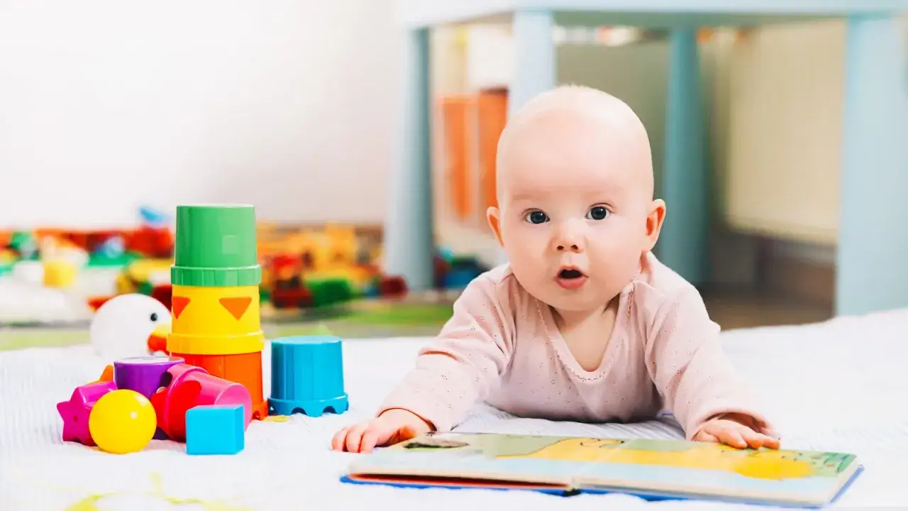 Niemowlę leży na brzuchu obok kolorowych zabawek sensorycznych i otwartej książeczki.