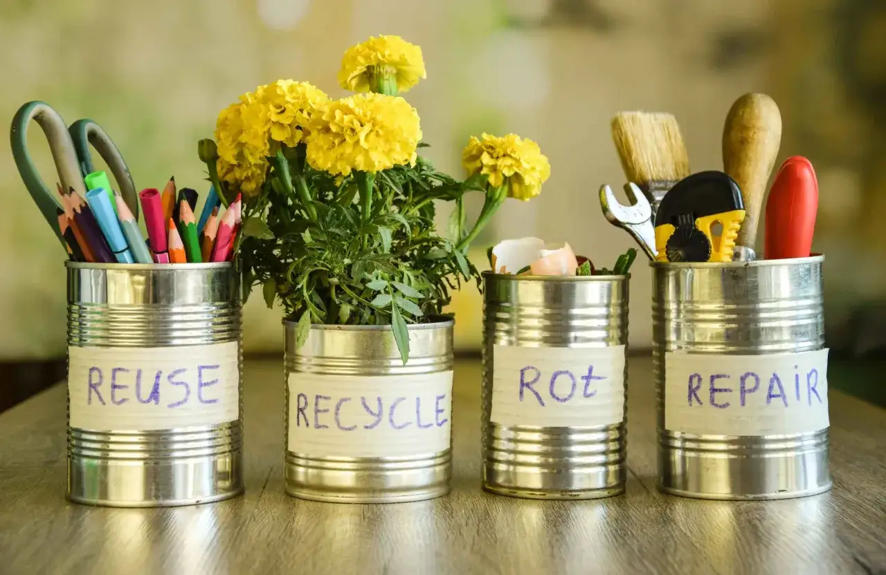 Puszki metalowe pokazują, co zrobić z odpadami: REUSE (nożyczki, kredki), RECYCLE (kwiaty), ROT (skorupki jajek), REPAIR (narzędzia).