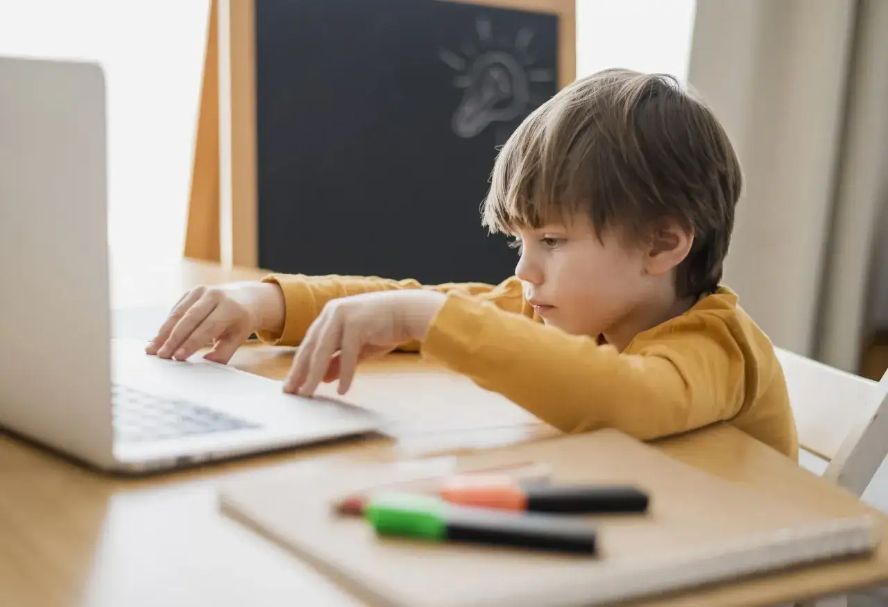 Chłopiec z problemami z koncentracją u dziecka siedzi przy laptopie, zamyślony. Na tablicy rysunek żarówki.