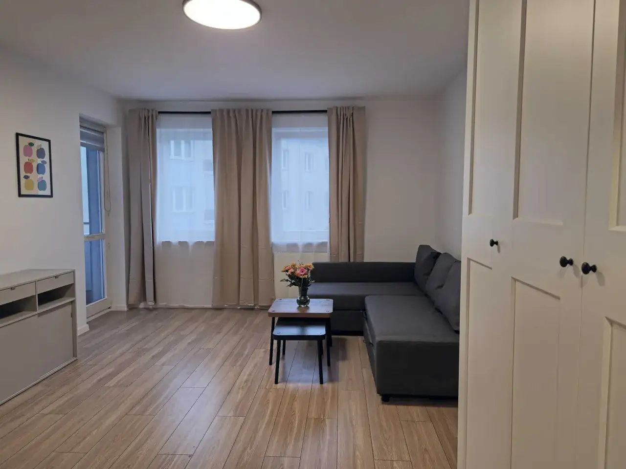 Nowoczesny salon z szarą kanapą, stolikiem kawowym z kwiatami i dużymi oknami.