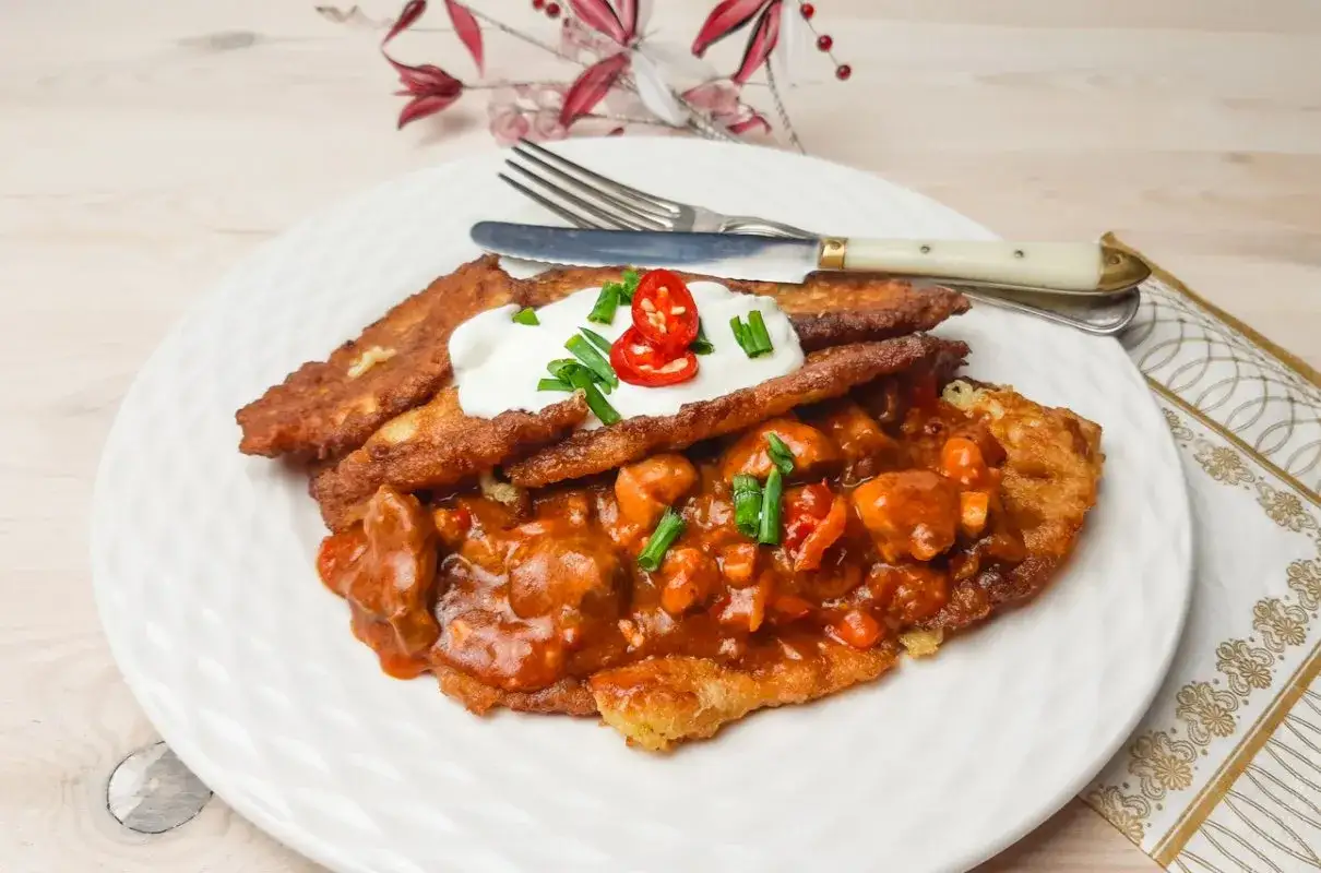 Pyszny placek po węgiersku z gulaszem, śmietaną i papryczką chili na białym talerzu.
