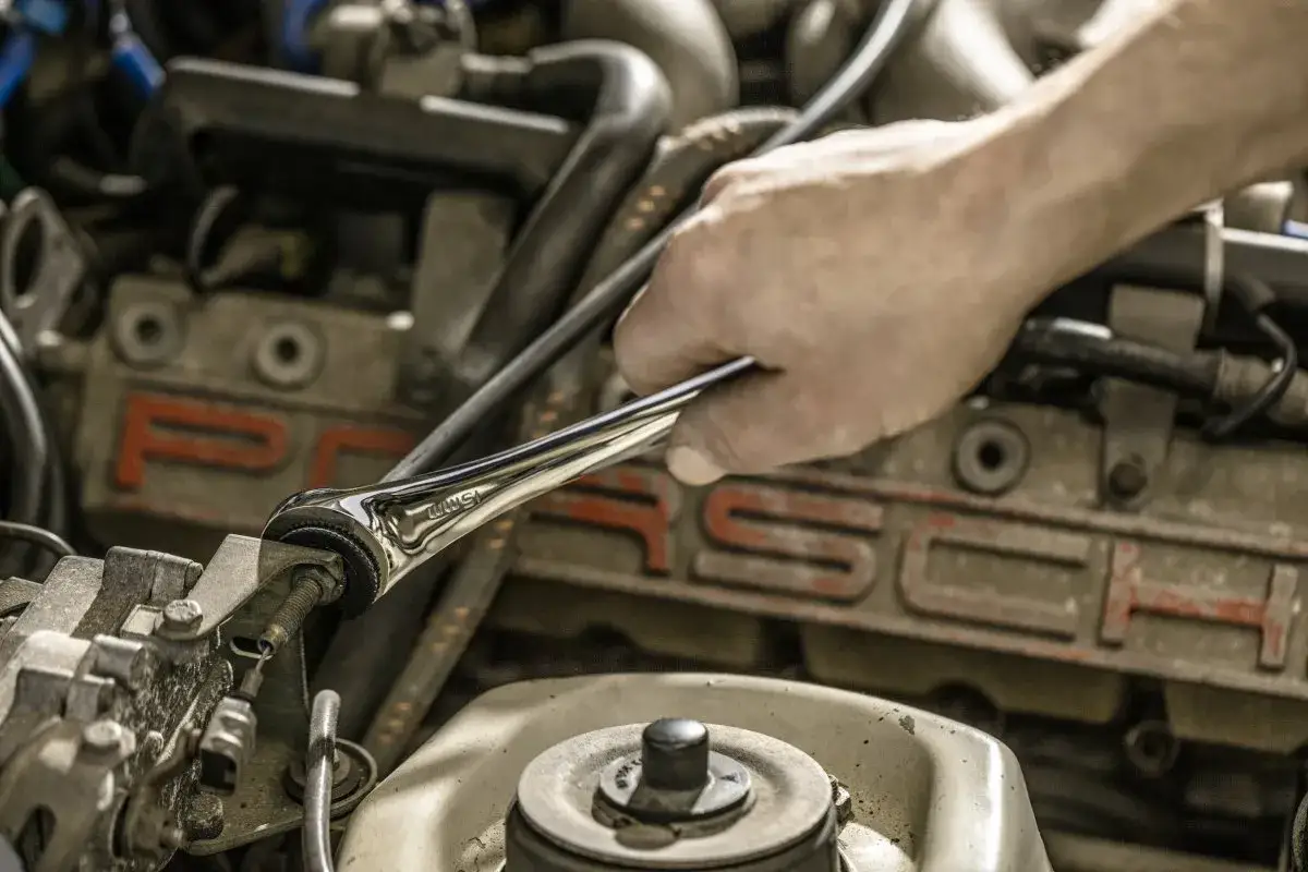 Ręka mechanika używa klucza motylkowego do dokręcania śruby w silniku Porsche.