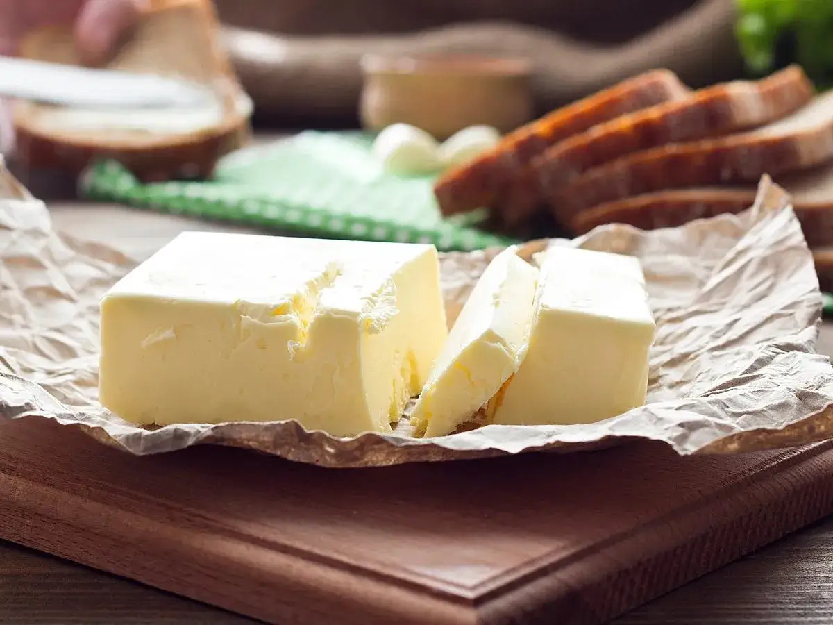 Masło na papierze, obok kromek chleba. Czy masło roślinne jest zdrowe? To pytanie zadaje sobie wiele osób.