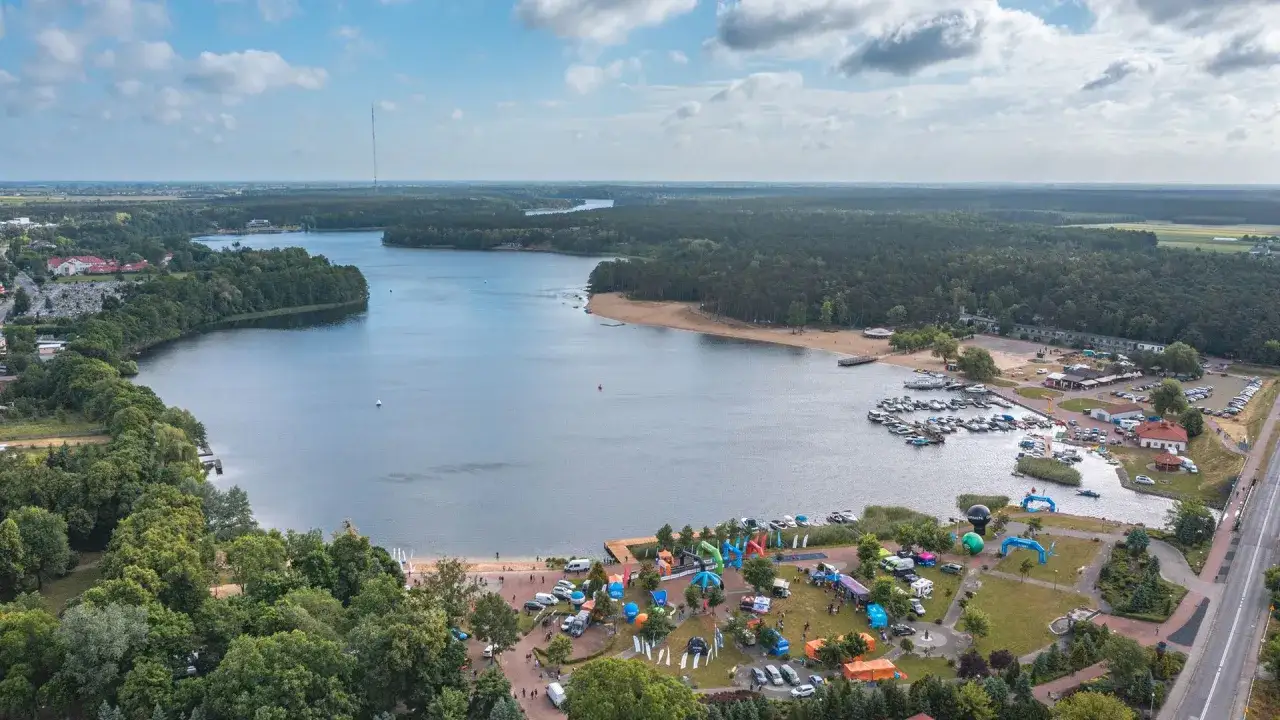 Widok na jezioro Otmuchowskie z lotu ptaka. Widać plażę, przystań jachtową, las i miasteczko z atrakcjami.