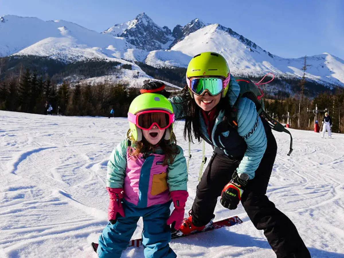 Mama i dziecko na stoku, dziewczynka ma narty dla 2 latka i jest podekscytowana.