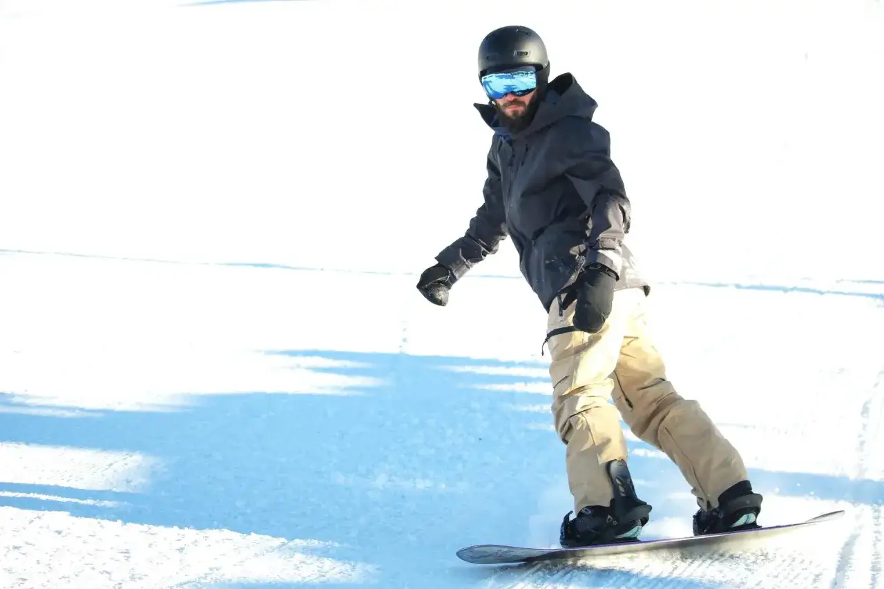 Mężczyzna w kasku i goglach zjeżdża na snowboardzie. Zastanawiasz się, ile kosztuje wypożyczenie snowboardu?