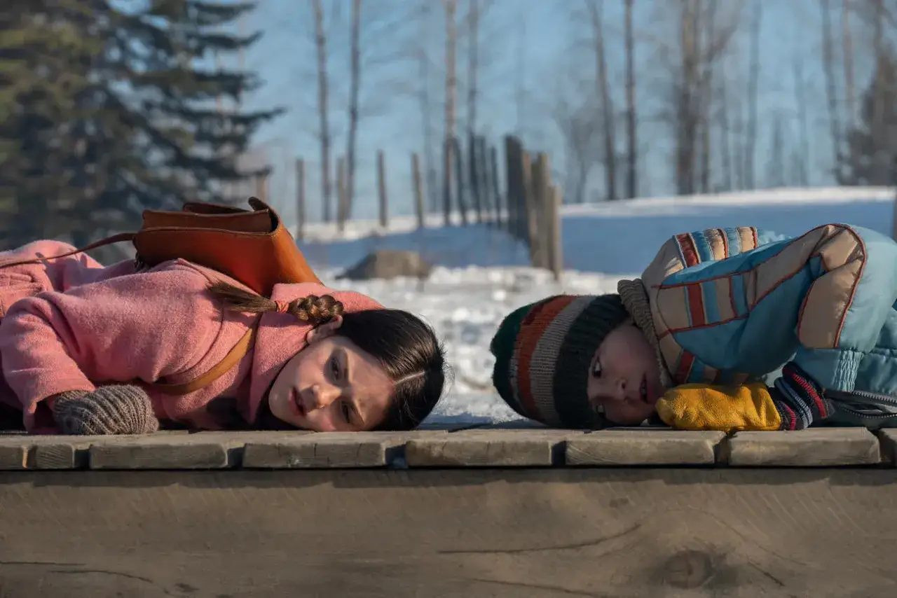 Dzieci leżą na drewnianej ławce, wpatrzone w dal. Ich twarze wyrażają zadumę, jakby snuły opowieści z pętli czasu, czekając na kolejne przygody.