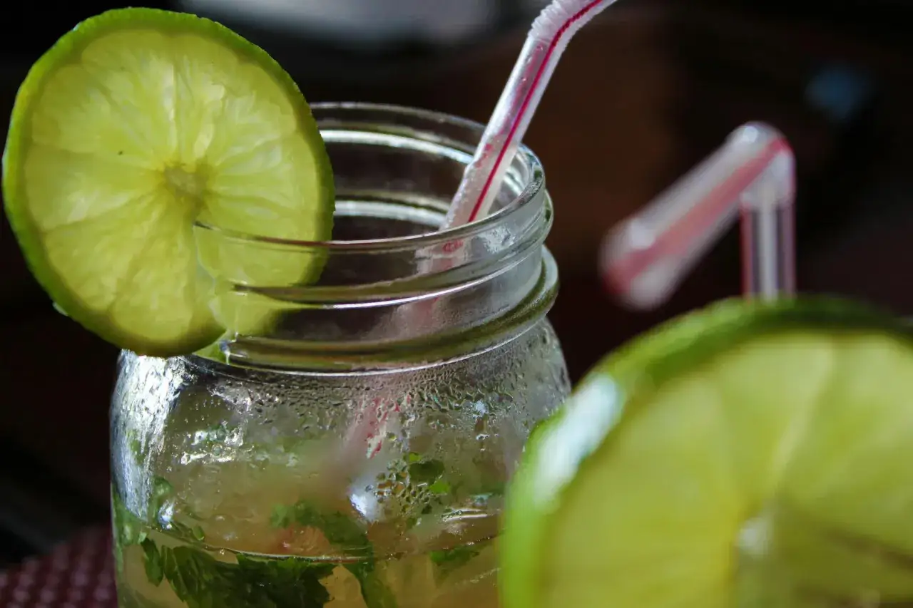 Orzeźwiający mohito drink, z widocznymi składnikami: limonką i miętą, w szklanym słoiku z rurką.