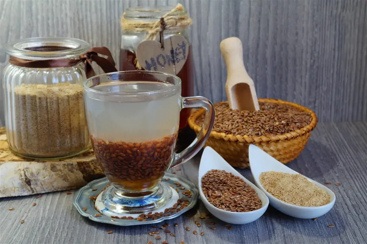 Naczynie z wodą i siemieniem lnianym do picia, obok słoik z mielonym siemieniem, koszyk z nasionami i miód.