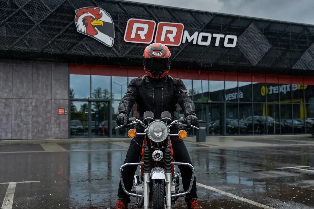 Motocyklista w kurtce z membraną, która chroni przed deszczem, przed budynkiem RR MOTO.