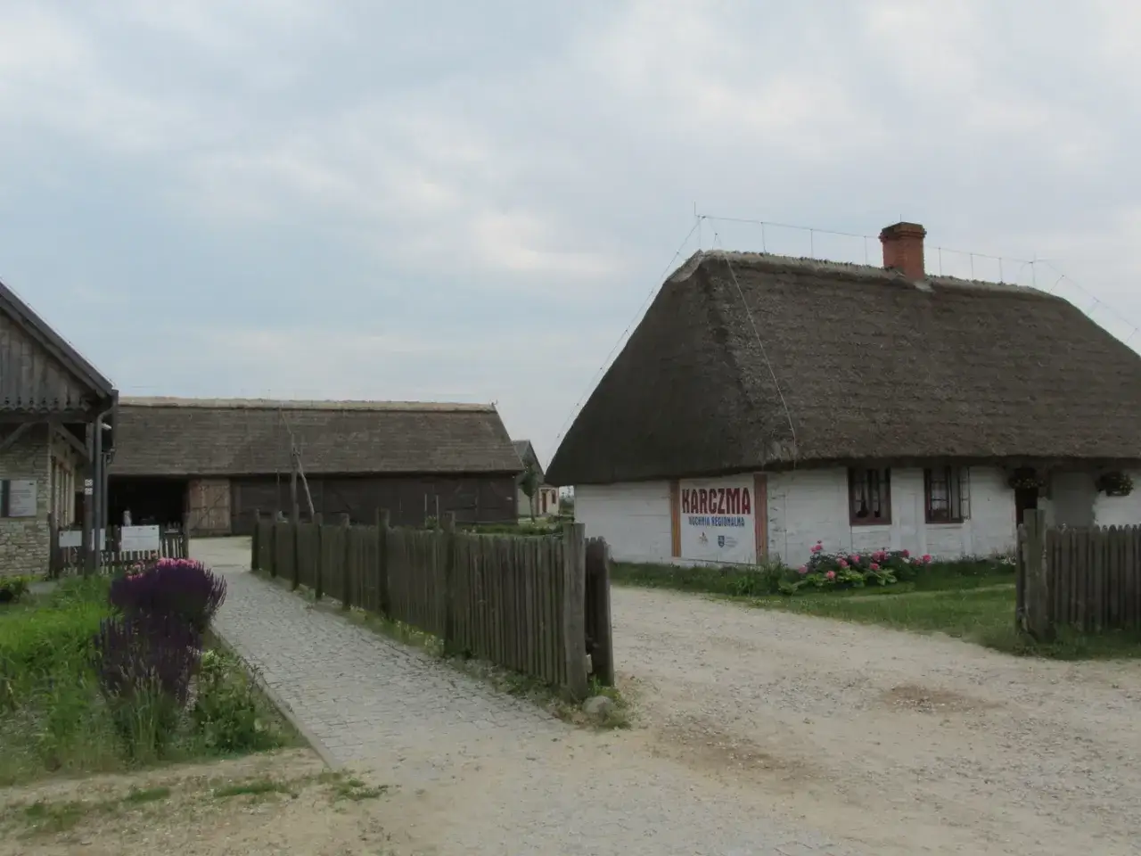 Zagroda Młynarska w Uniejowie: biały budynek z karczmą, drewniane zabudowania i ścieżka.