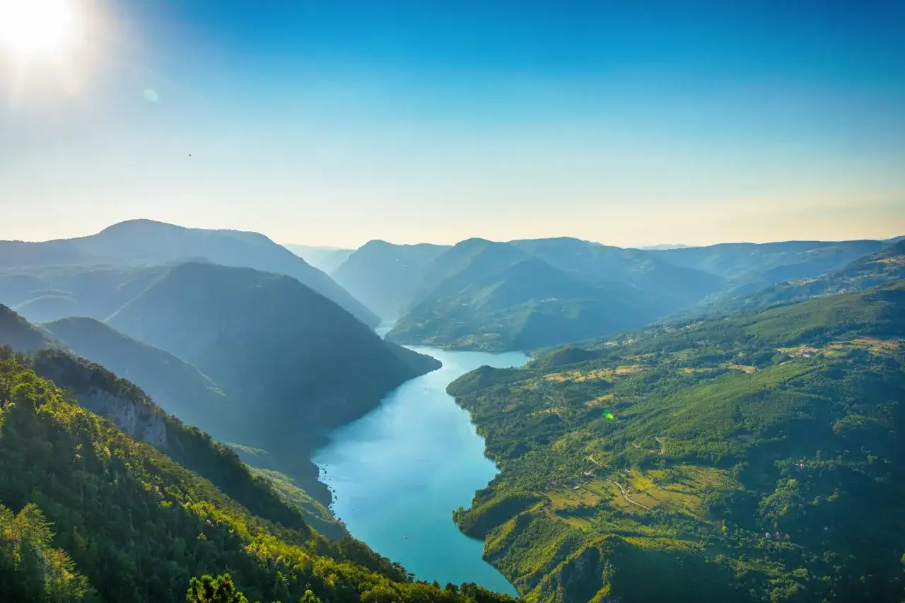Malowniczy widok na rzekę wijącą się między zielonymi wzgórzami Serbii. Słońce oświetla szczyty gór, tworząc głębokie cienie.