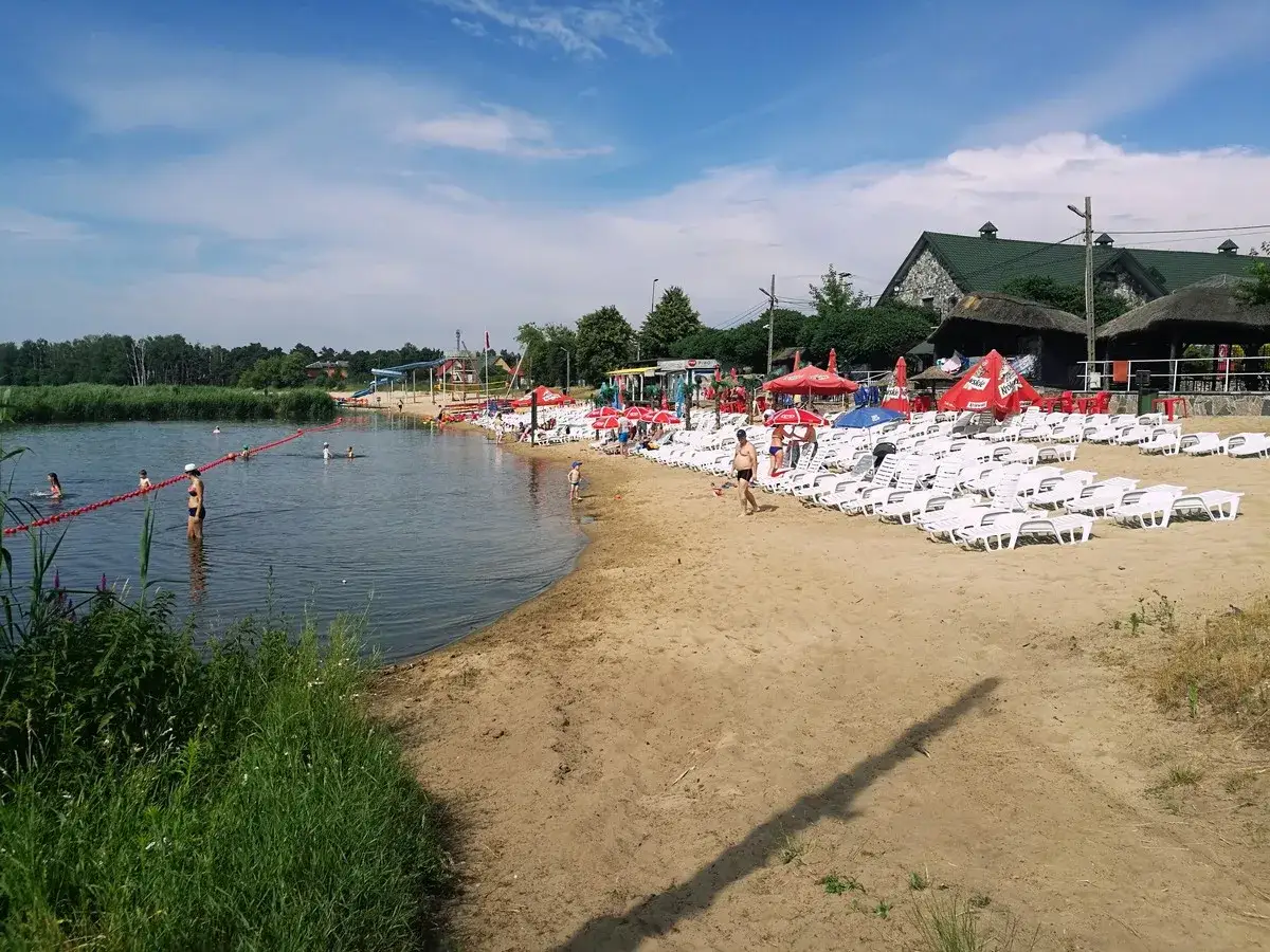 Słoneczny dzień na plaży, gdzie łowisko wilga wodna kraina zaprasza do kąpieli i relaksu. Leżaki i parasole czekają na plażowiczów.