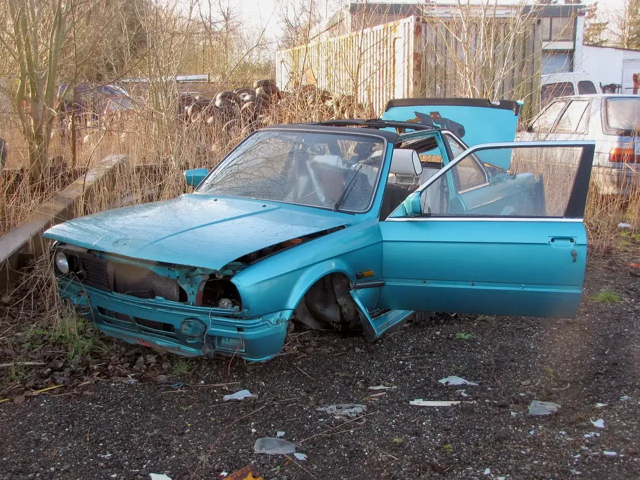 Turkusowy, zniszczony samochód na złomowisku. Drzwi i maska otwarte, jakby ktoś właśnie zaczął zastanawiać się, jak zezłomować auto.