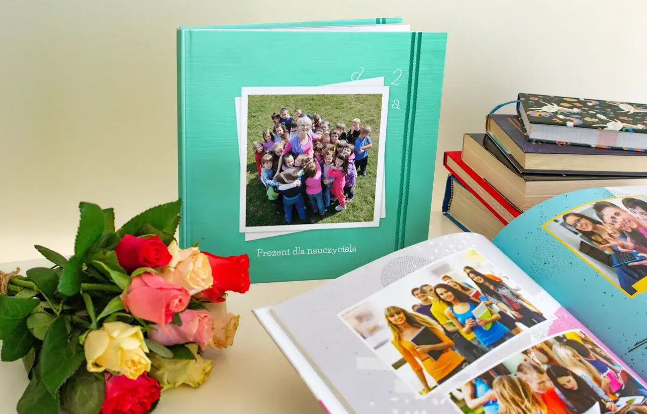 Album ze zdjęciami dzieci i nauczycielki, bukiet róż i stos książek.