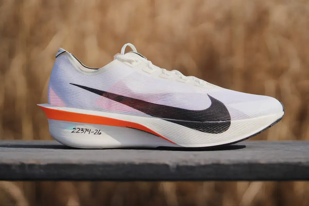 Białe buty treningowo startowe Nike z czarnym logo. Pomarańczowe akcenty i numeracja na podeszwie.