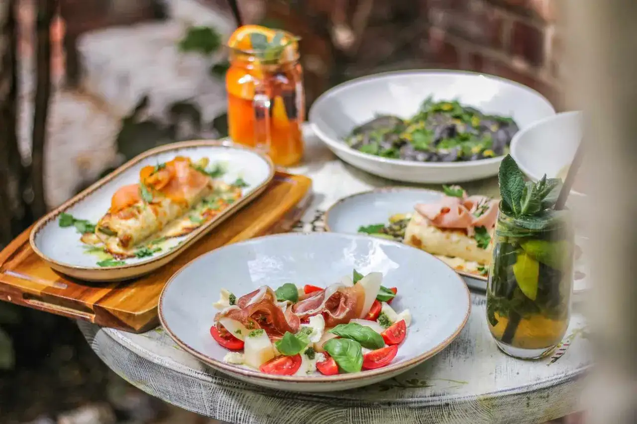 Stół z daniami: naleśniki z łososiem, sałatka z szynką parmeńską i pomidorkami, czarne spaghetti, napoje.