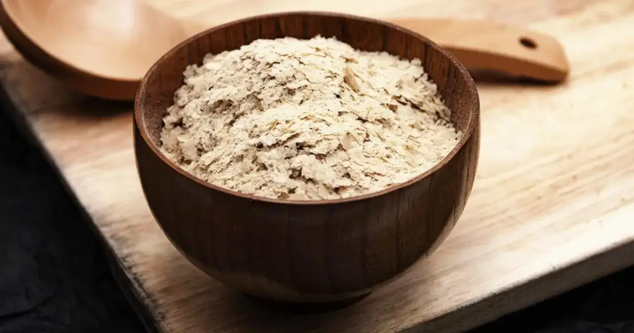 Płatki drożdżowe w drewnianej misce. Odpowiedź na pytanie: czy drożdże są wegańskie? Tak, płatki drożdżowe są wegańskie.