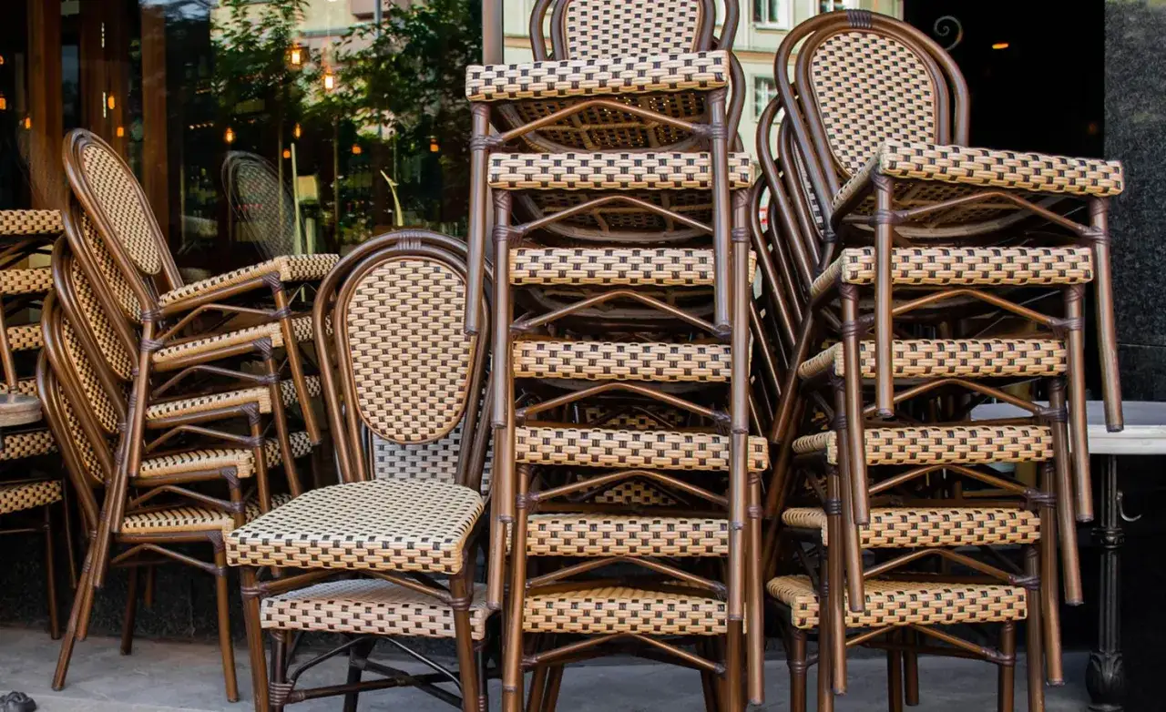 Gestapelte braune Bistrostühle mit geflochtenen Sitzflächen und Rückenlehnen vor einem Restaurant.