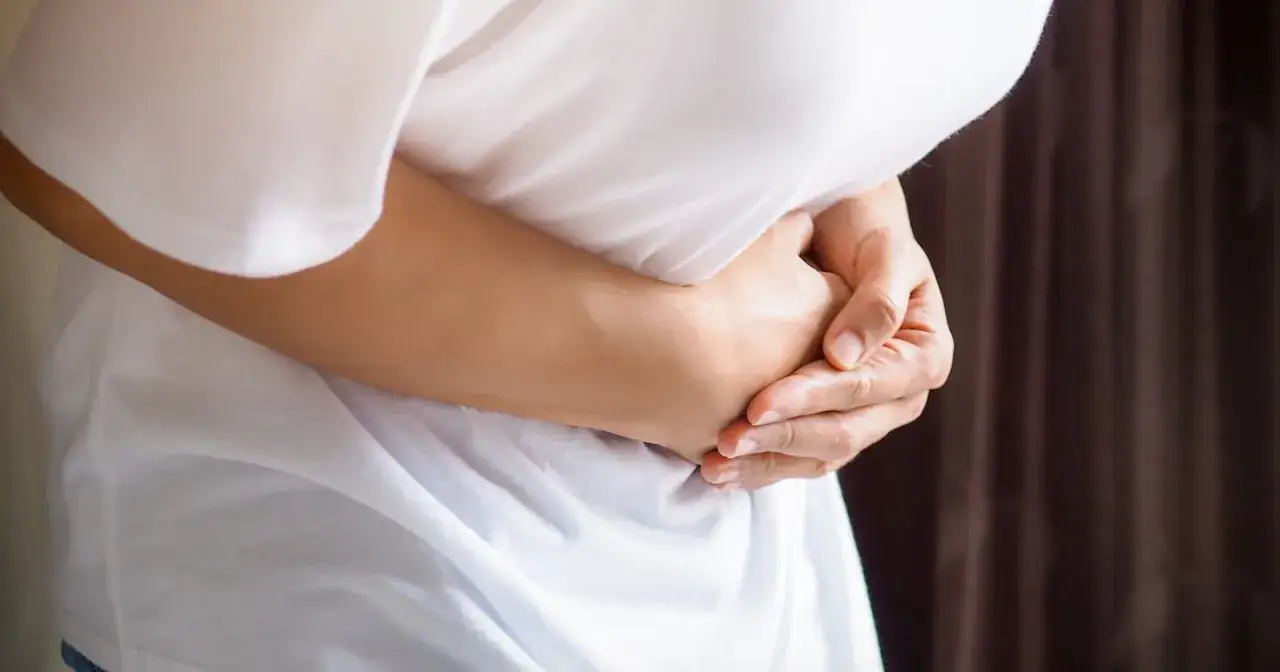 Osoba trzyma się za brzuch, odczuwając ostry ból w lewym boku.